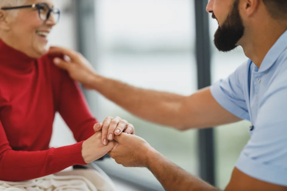 A health care worker holds an older woman's hand to reassure her